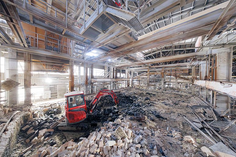 A view inside the melting furnace after the roof and walls have been dismantled. An excavator is clearing away the material from the dismantling work.